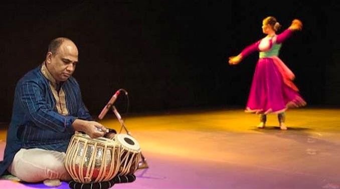 A man playing the Tabla and a woman dancing a traditional Indian dance