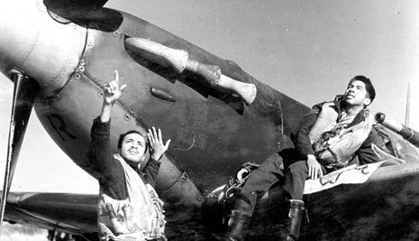 Two pilots resting against the exterior of an old style plane.