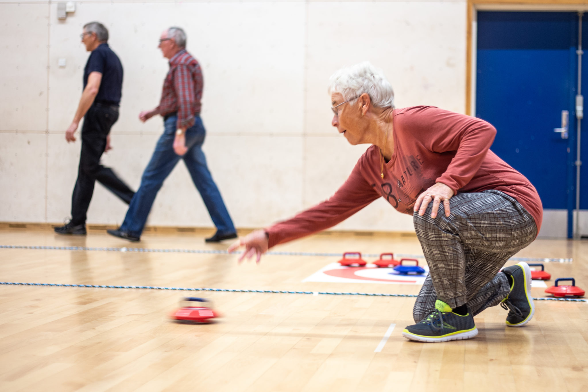 Person kneeling forward delivering a kurling 'stone'