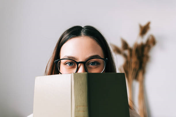 A woman peering over the top of an open book