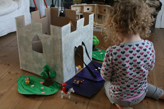 Small child seated on floor in front of a castle made of cardboard