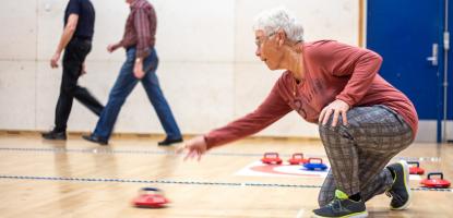 Person kneeling forward delivering a kurling 'stone'