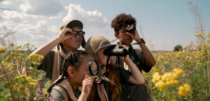 Four children with binoculas in field